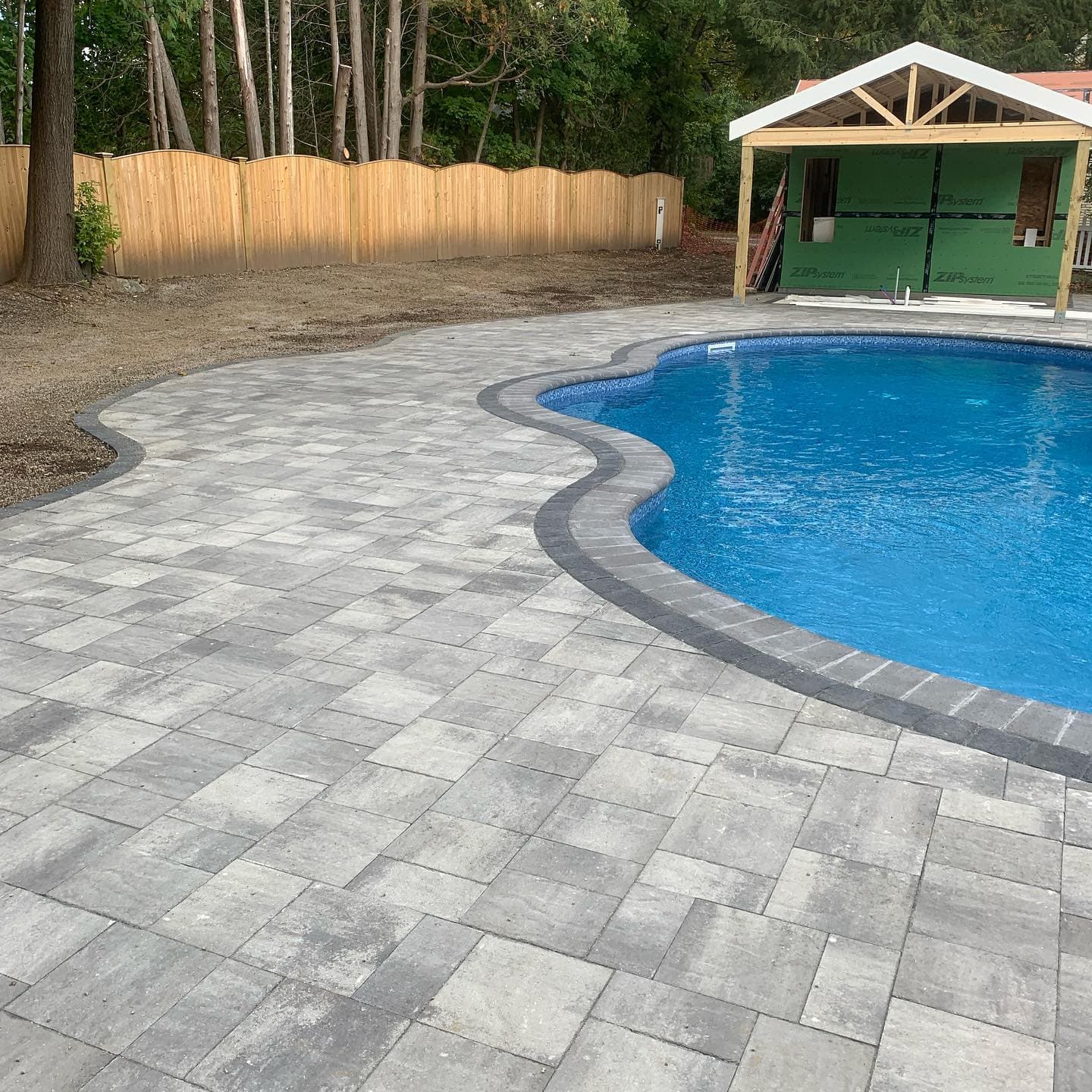 Kidney-shaped pool with a gray paver deck