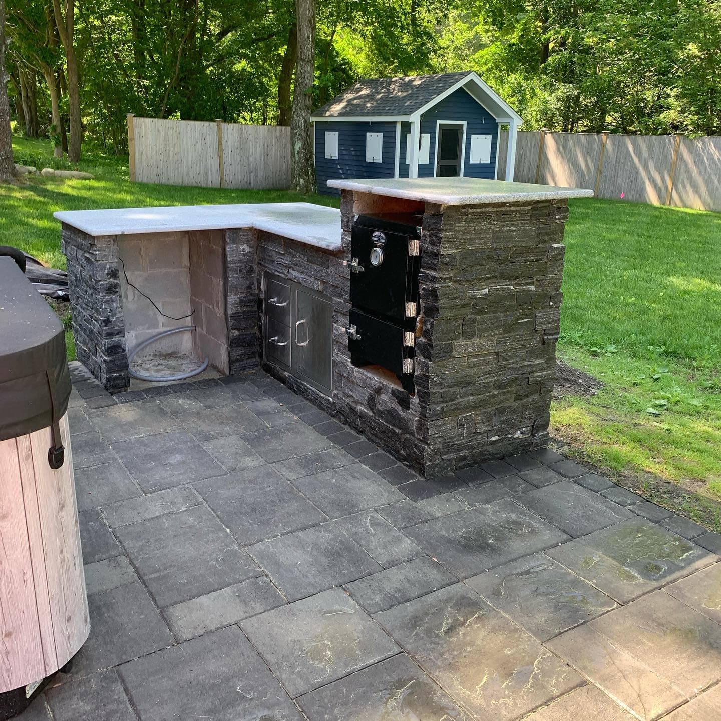L-shaped stacked-stone outdoor kitchen on a paver patio